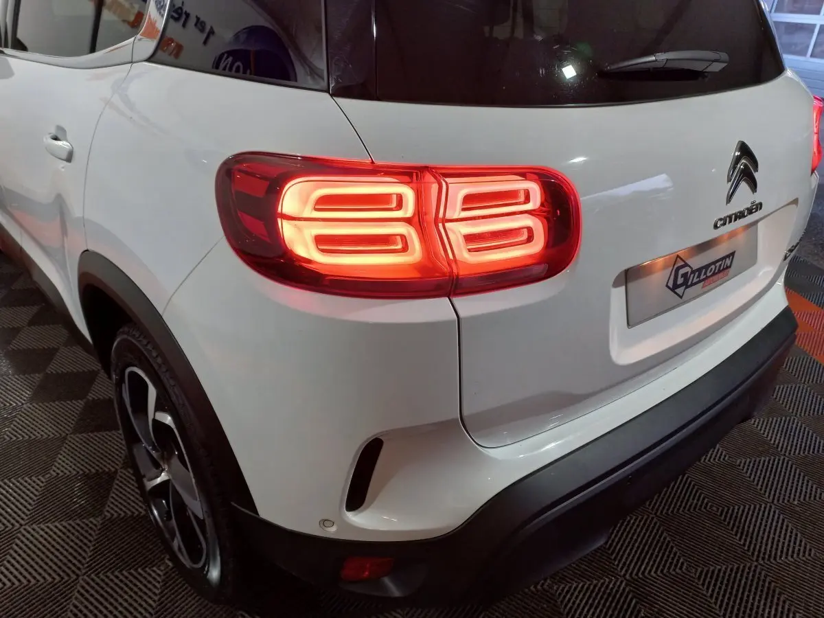 Vue 3/4 arrière gauche d'un Citroën C5 Aircross blanc avec feux arrière LED allumés et logo Citroën visible.