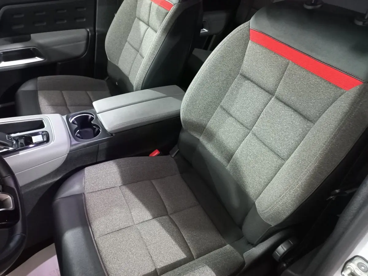 Vue intérieure rapprochée des sièges avant gris avec bande rouge sur appuie-tête du Citroën C5 Aircross blanc.