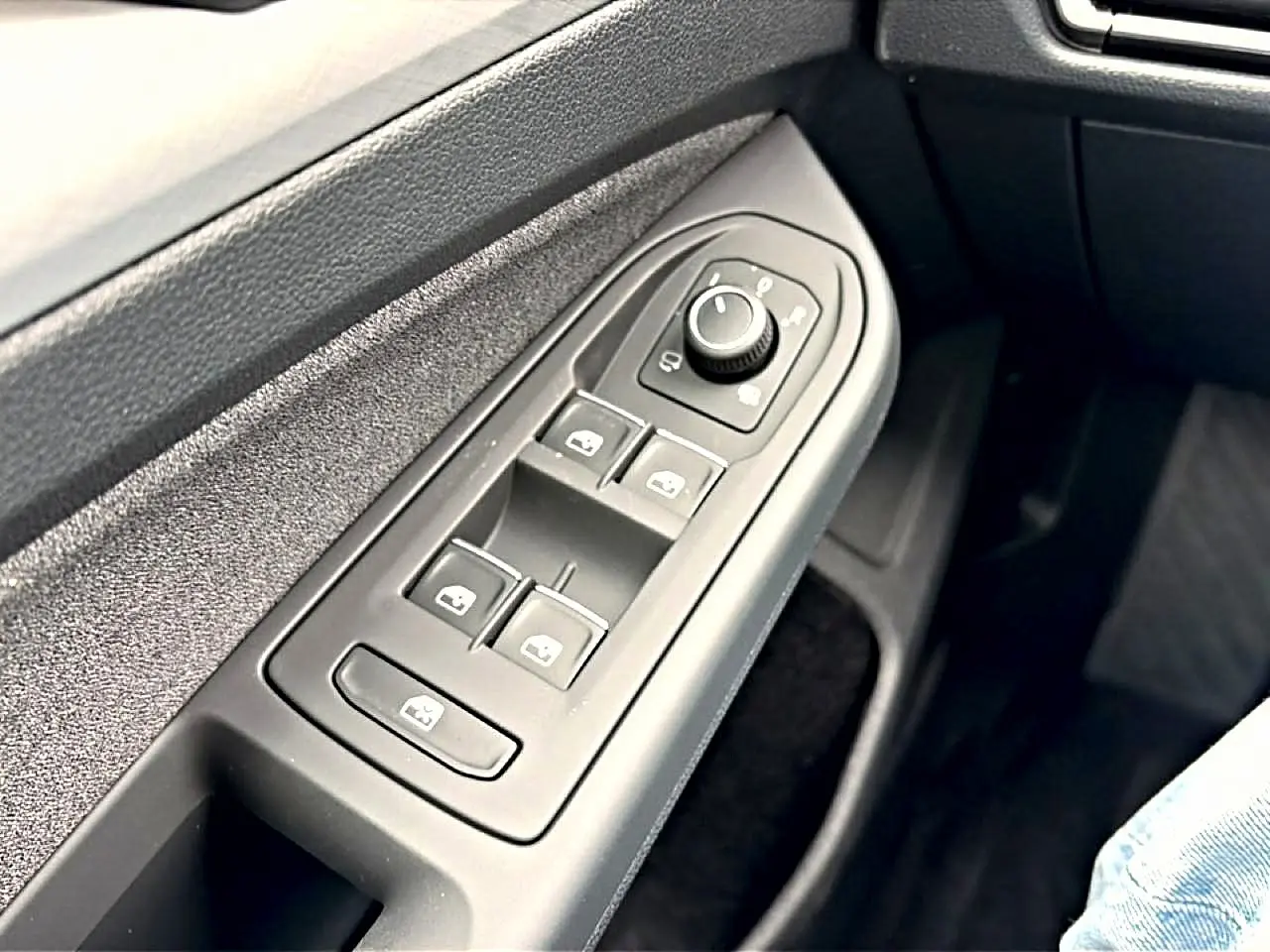 Gros plan sur les commandes électriques des vitres et rétroviseurs côté conducteur d'une Volkswagen Golf bleu glacier.