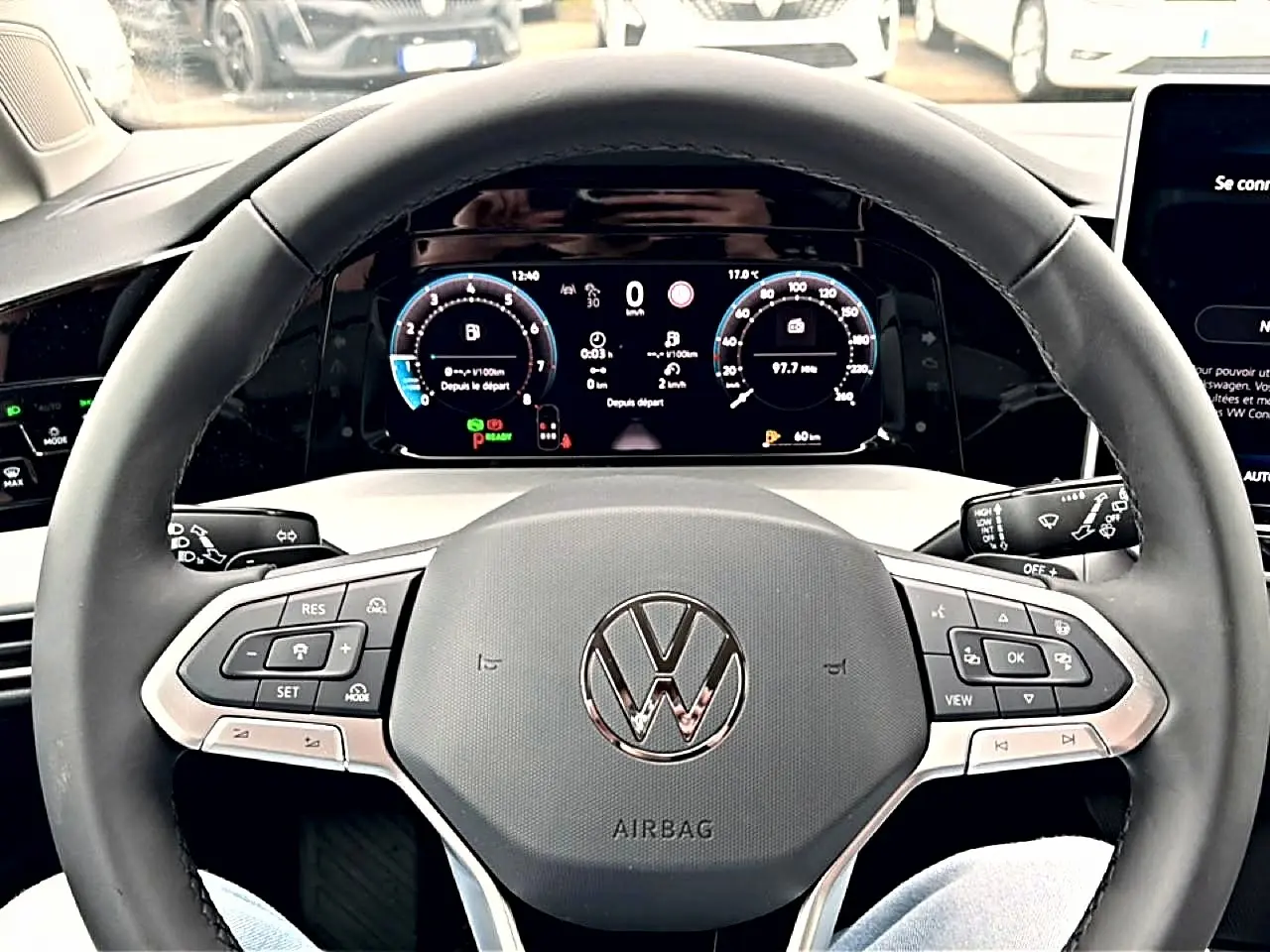 Vue rapprochée du volant noir d'une Volkswagen Golf 2026 avec tableau de bord digital et commandes intégrées.