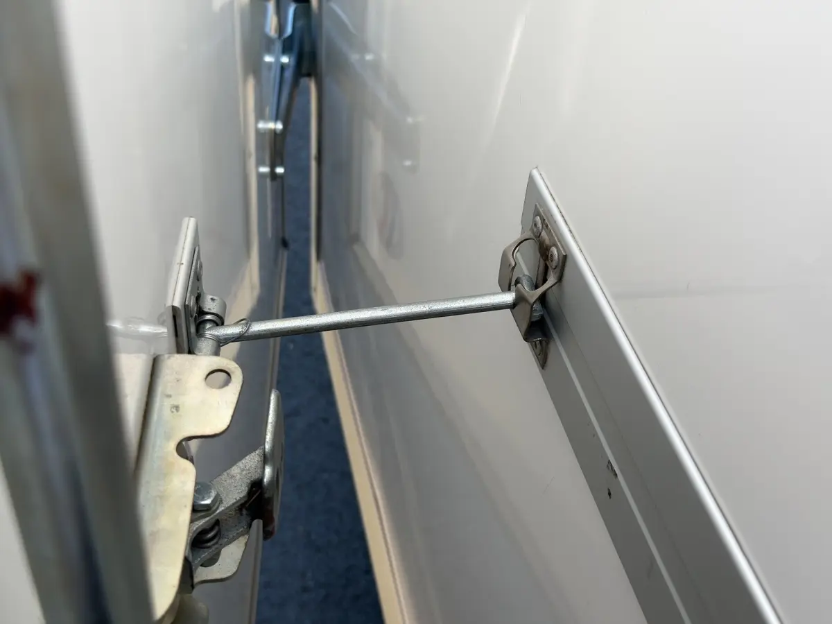 Détail du mécanisme d’ouverture métallique sur la porte arrière blanche du Renault Master 2024.