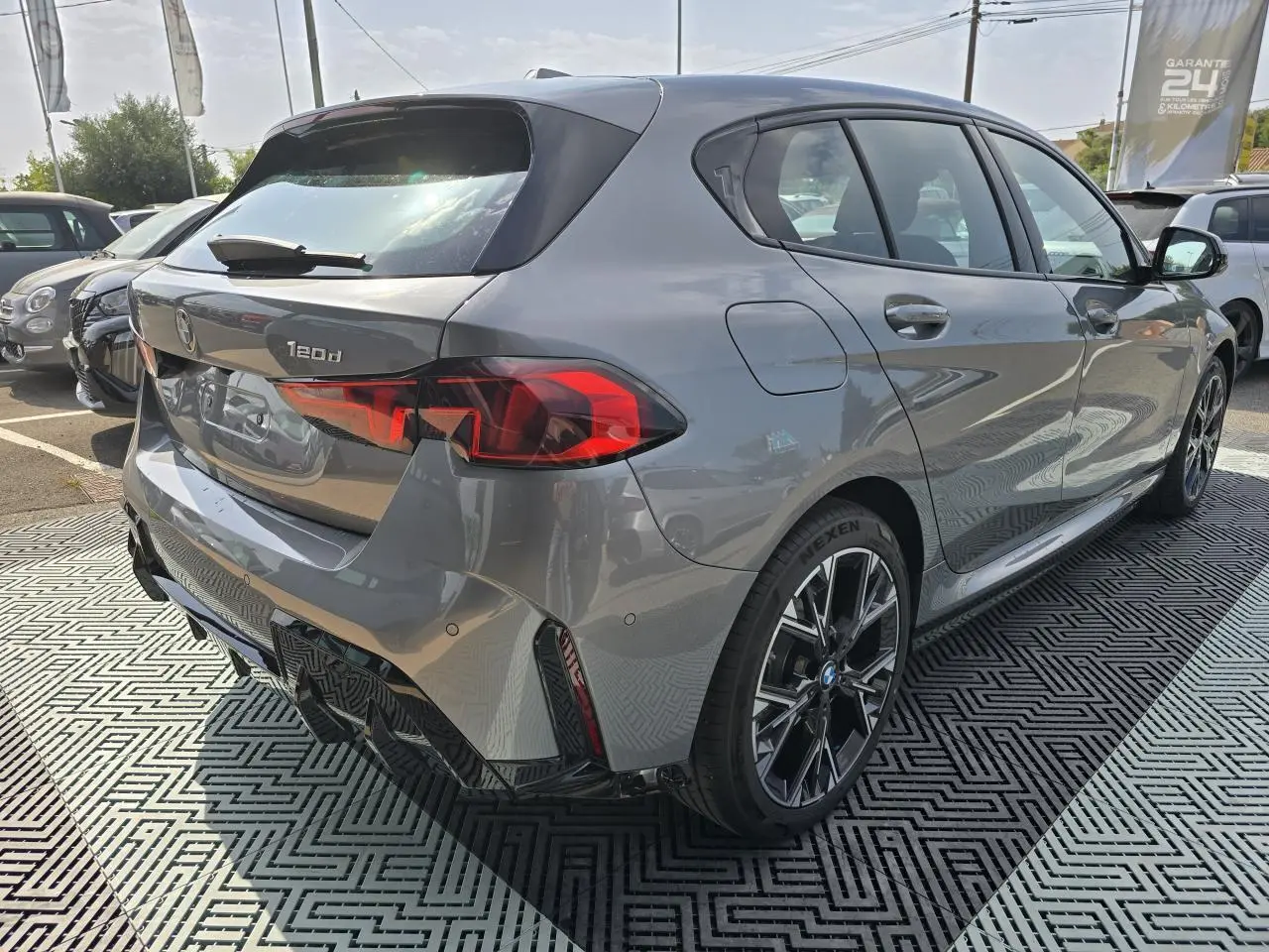 BMW Série 1 120d gris Skyscraper vue 3/4 arrière droit avec jantes M Sport et feux arrière LED distinctifs.