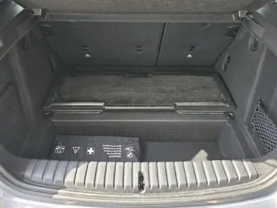 Coffre ouvert d'une BMW Série 1 F70 120d gris Skyscraper, montrant un espace de chargement propre avec filet latéral et trousse de secours.