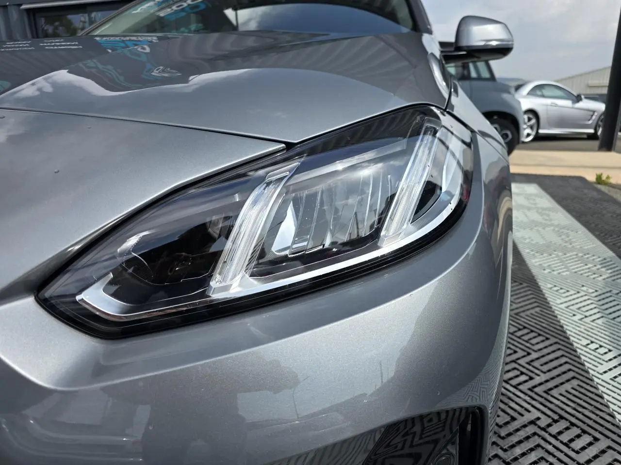 Gros plan sur le phare avant droit d'une BMW Série 1 120D 2024 en gris Skyscraper métallisé.