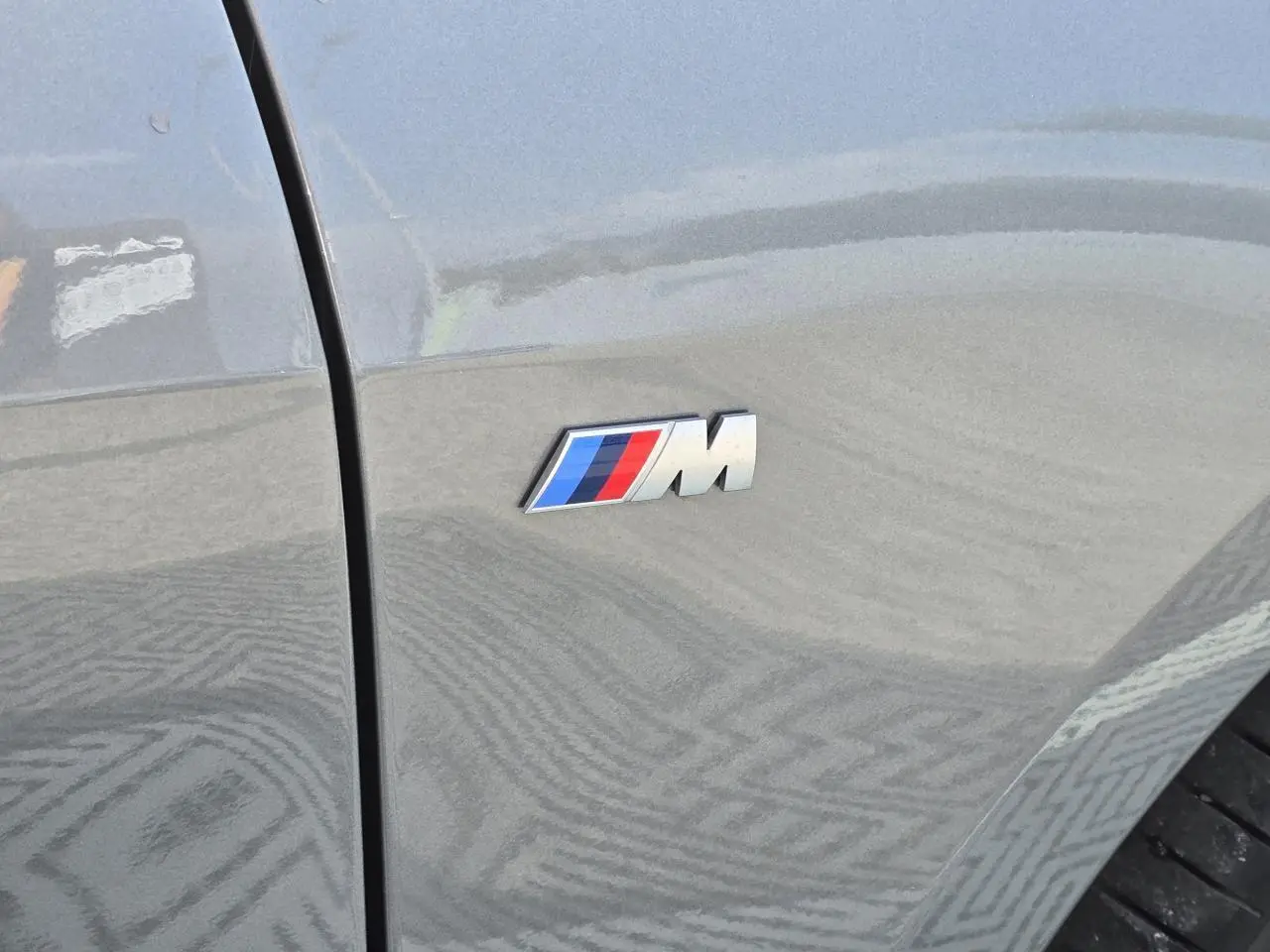 Gros plan sur l'emblème M sur l'aile avant droite d'une BMW Série 1 gris Skyscraper 2024.