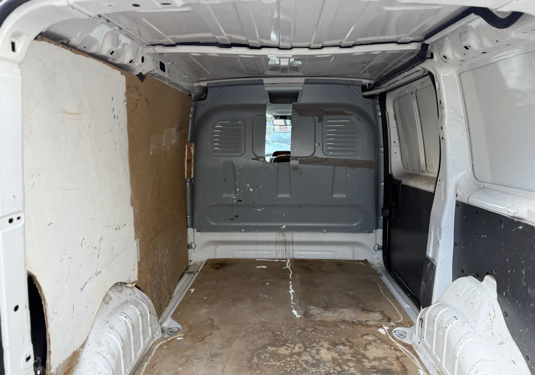 Vue intérieure arrière du fourgon blanc FIAT Scudo 1.6 HDI 90 de 2015, montrant l'espace de chargement usé et la cloison métallique grise.