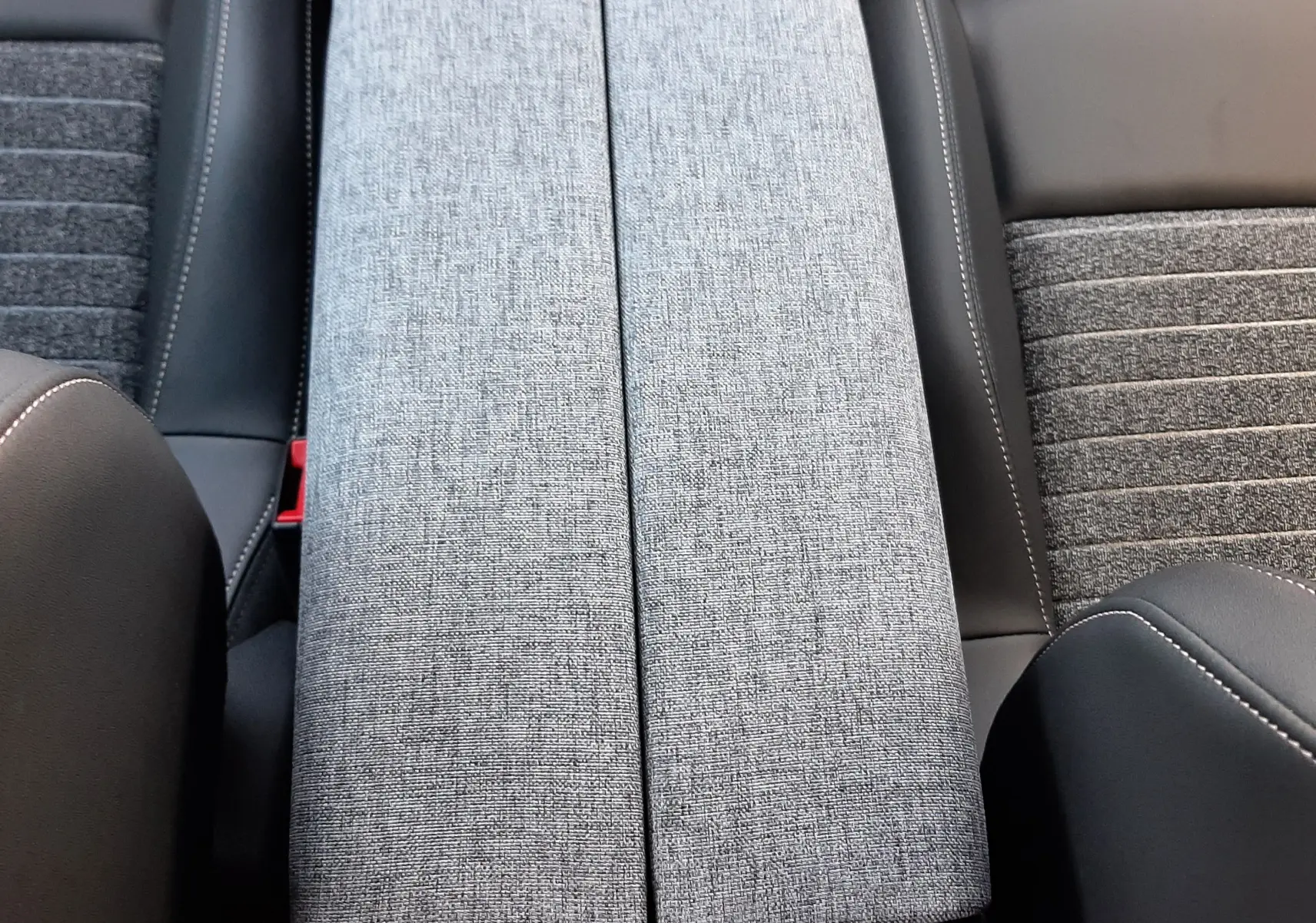 Gros plan sur l'accoudoir central en tissu gris et les sièges bi-matière noir et gris du Peugeot 5008 hybride 2025.