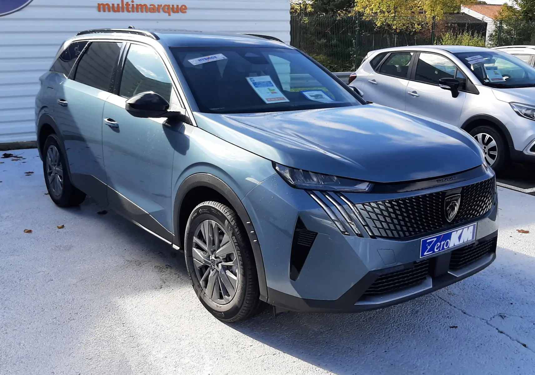 Peugeot 5008 bleu Ingaro en 3/4 avant droit, SUV hybride avec calandre noire distinctive et jantes alliage.