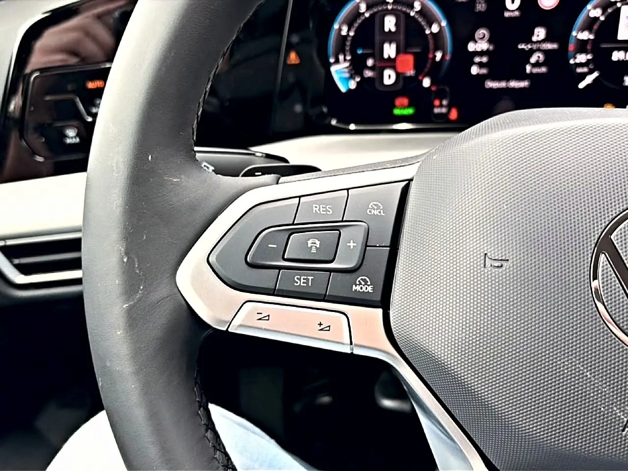 Gros plan sur le volant noir de la Volkswagen Golf 2026 avec commandes intégrées et tableau de bord numérique en arrière-plan.