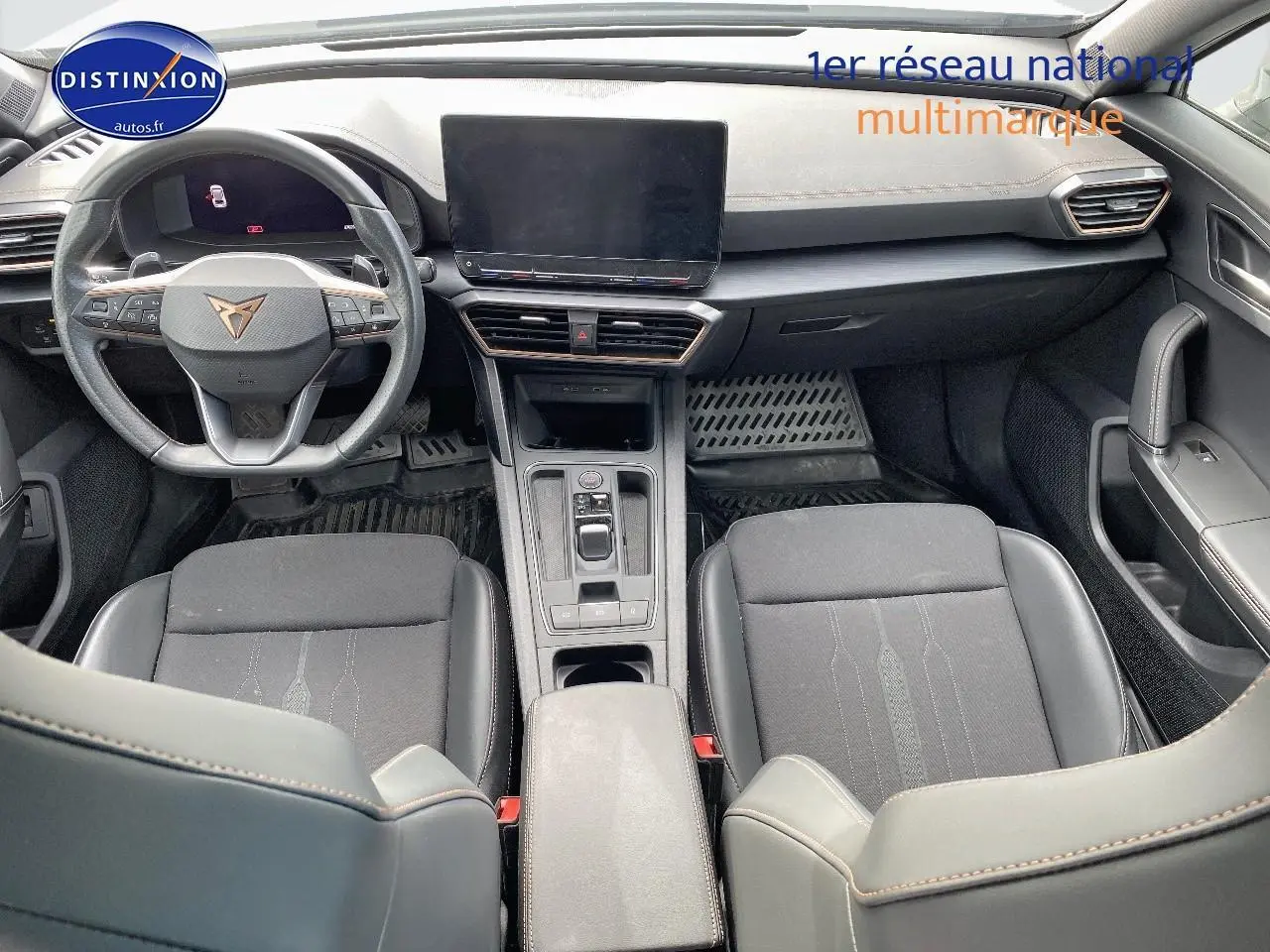 Vue intérieure avant du CUPRA Formentor 2023, sièges noirs tissu et similicuir, volant sport avec logo CUPRA, écran tactile central.