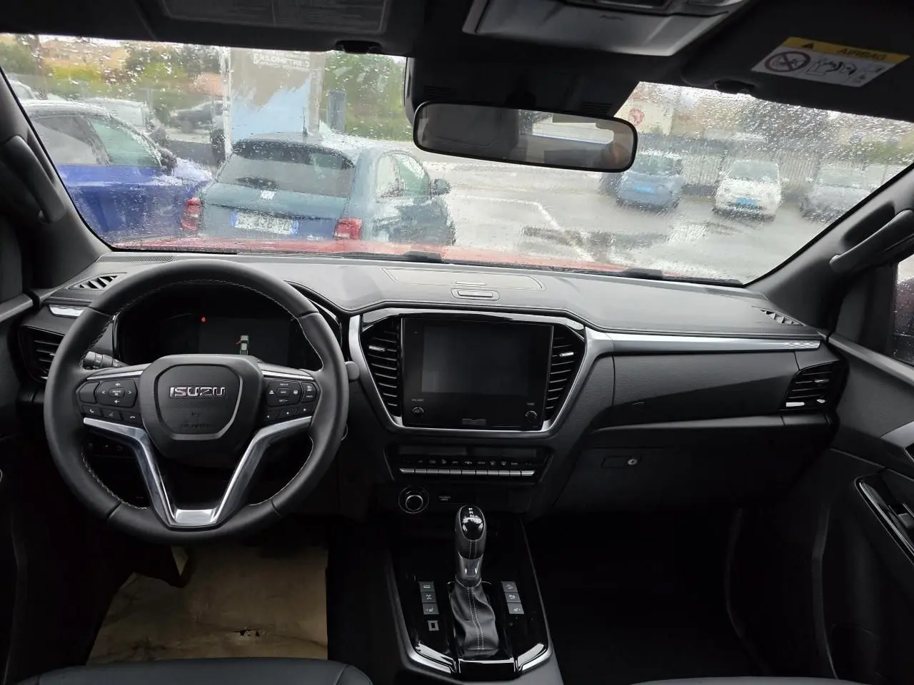 Intérieur noir du pick-up Isuzu D-MAX 2025 vu de face, avec volant cuir et écran tactile central éteint.