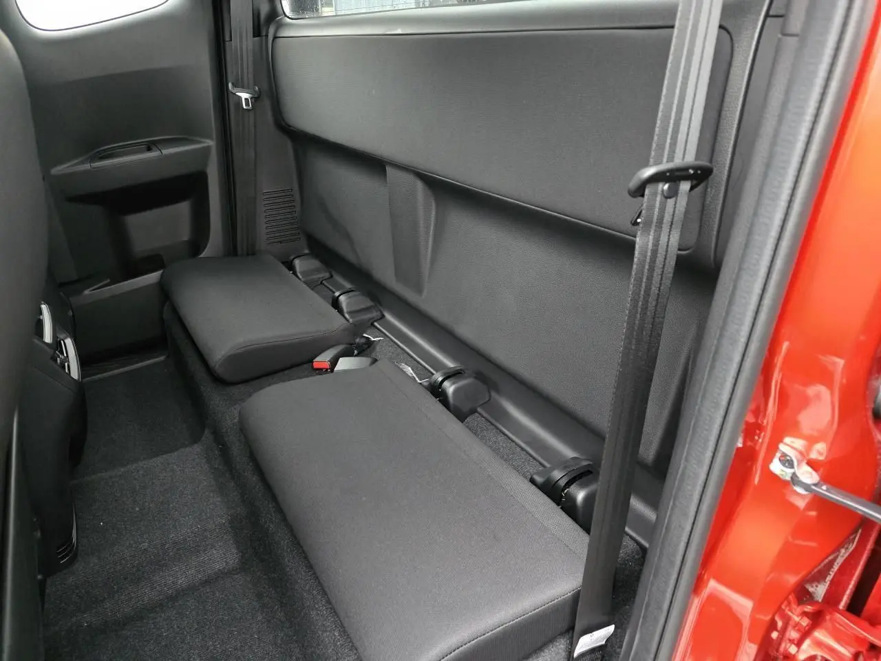 Vue latérale intérieure du siège arrière rabattable noir du pick-up Isuzu D-MAX orange métallisé, porte ouverte côté droit.