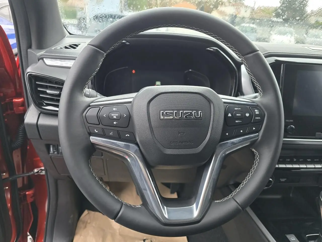 Volant en cuir avec commandes multifonctions de l'Isuzu D-MAX 2025, intérieur côté conducteur visible en orange métallisé.