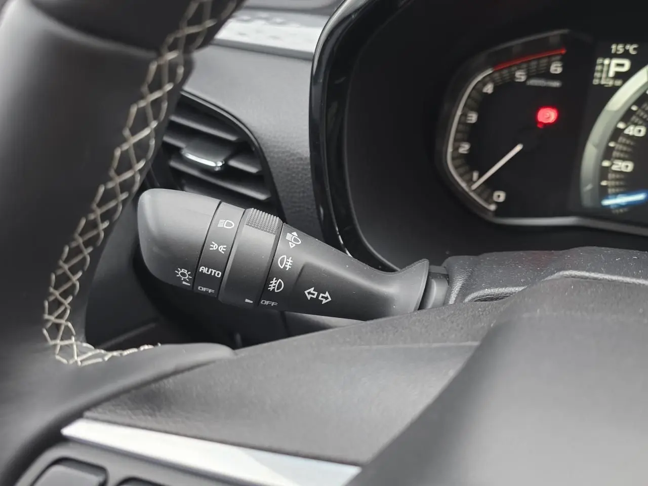 Gros plan sur la commande des phares et clignotants noire, tableau de bord et volant en cuir gris d'un Isuzu D-MAX orange métallisé.