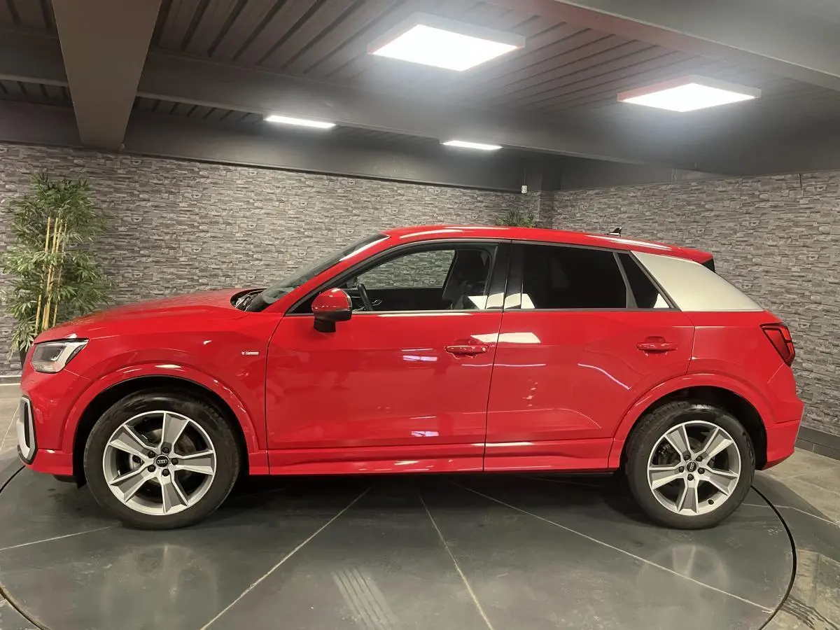 Audi Q2 S line rouge vue de profil côté gauche avec toit contrasté blanc et jantes sport 5 branches.