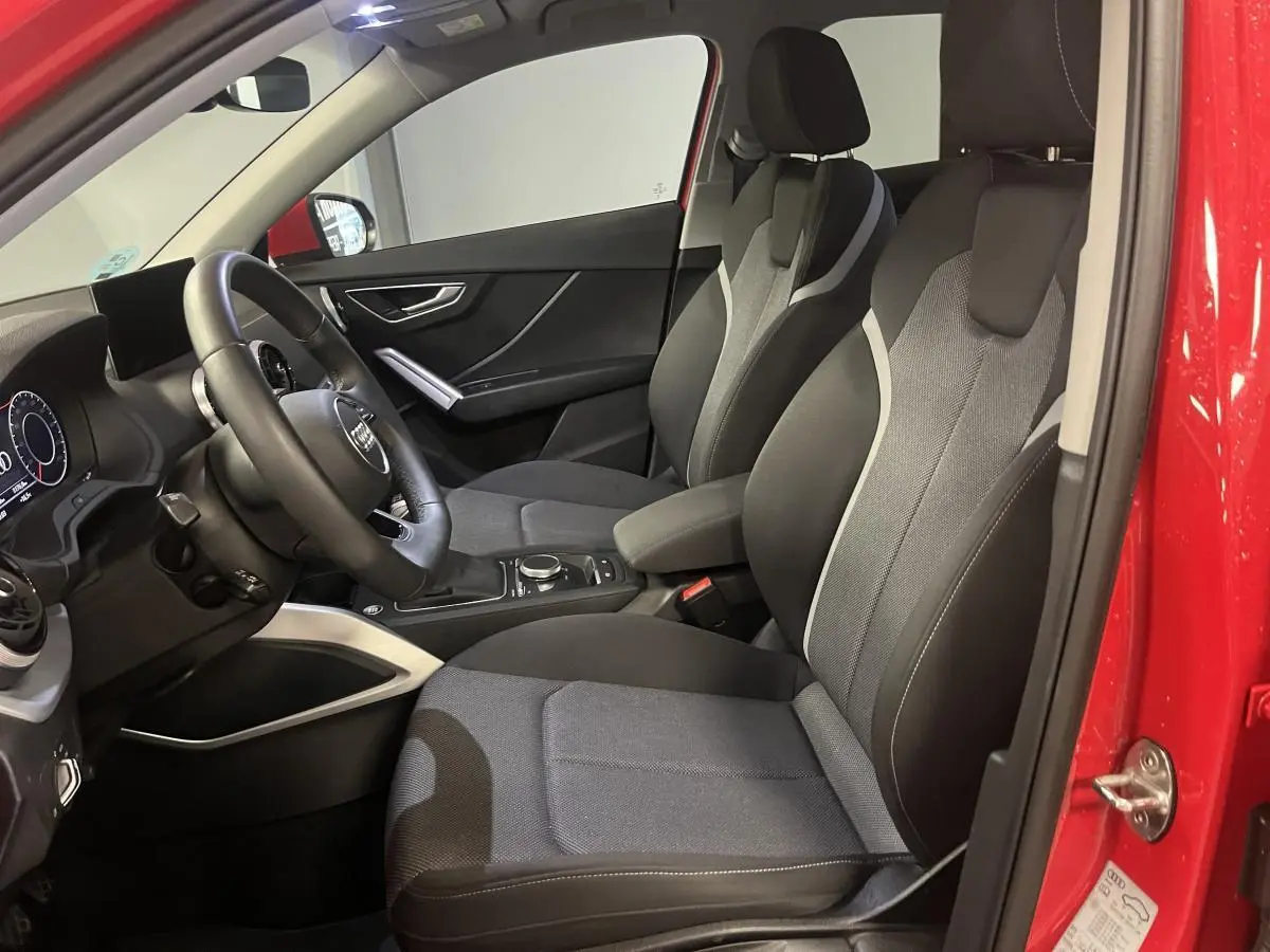 Intérieur avant droit d'un Audi Q2 rouge 2024 avec sièges tissu noir et gris et volant multifonction cuir.