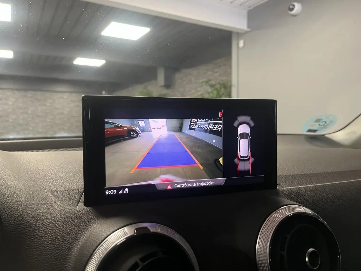 Écran intérieur affichant la caméra de recul et l'aide au stationnement du tableau de bord d'un Audi Q2 rouge.