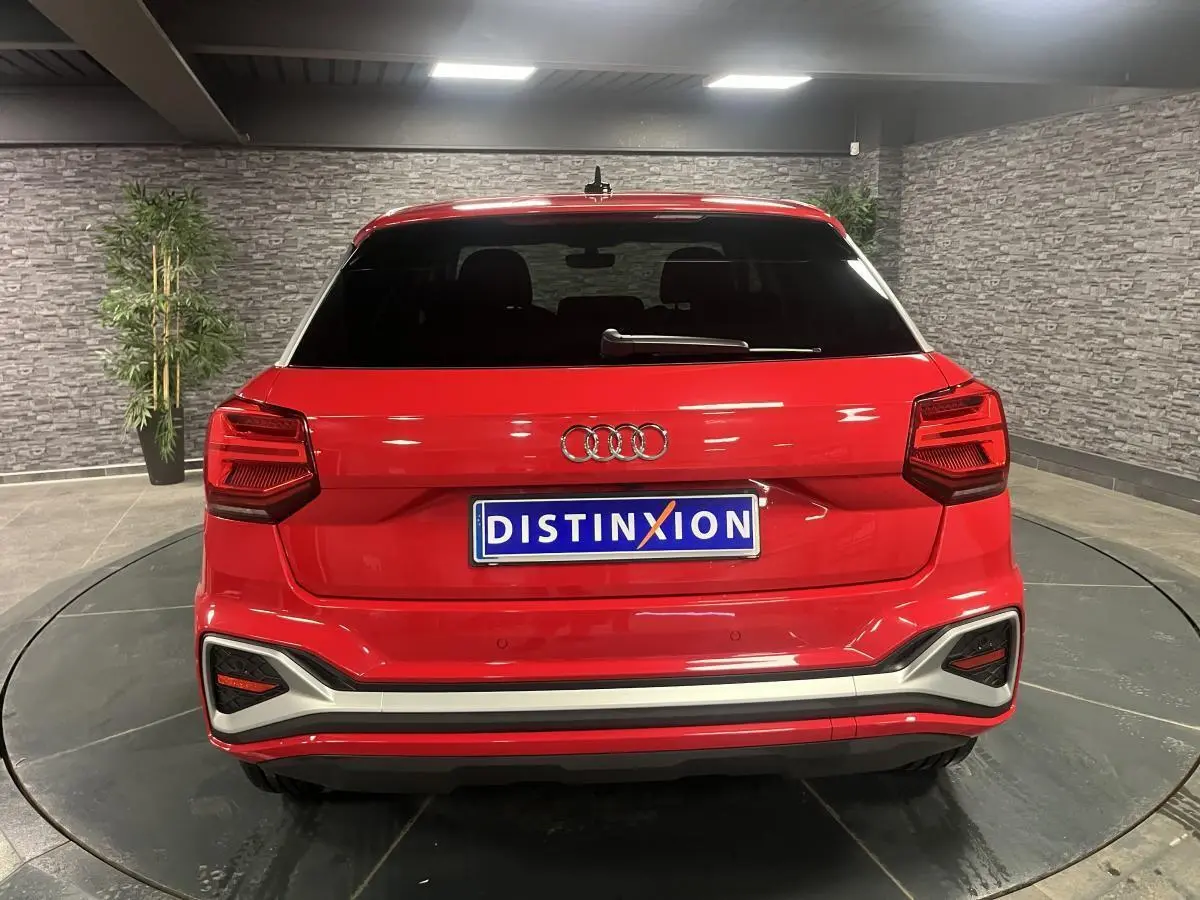 Vue arrière d'un Audi Q2 rouge 2024 avec hayon électrique et feux arrière LED dans un showroom.