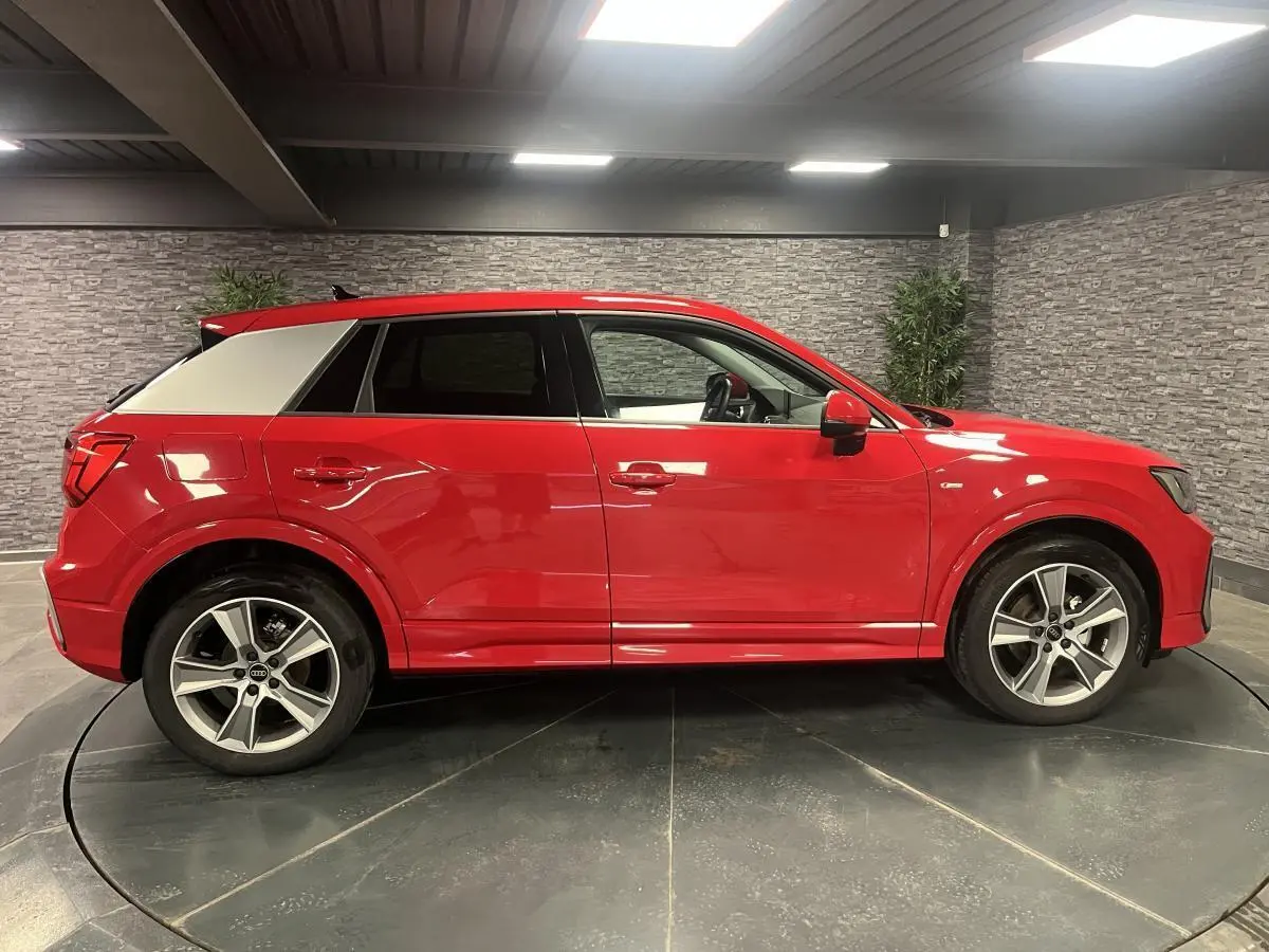 Profil côté gauche d'un Audi Q2 rouge 2024 avec jantes sport 5 branches et toit contrasté gris clair.