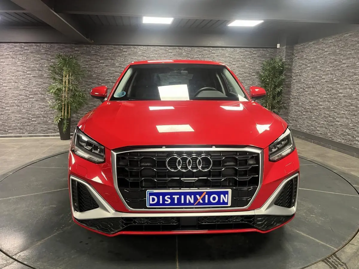 Vue frontale d'un Audi Q2 rouge S line 2024 avec calandre noire et détails argentés en intérieur showroom.