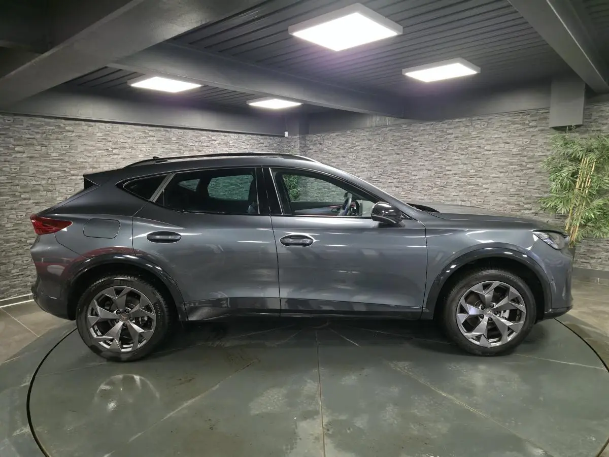 Vue de profil côté gauche du CUPRA Formentor gris métallisé avec jantes alliage 18'' et toit noir dans un garage.