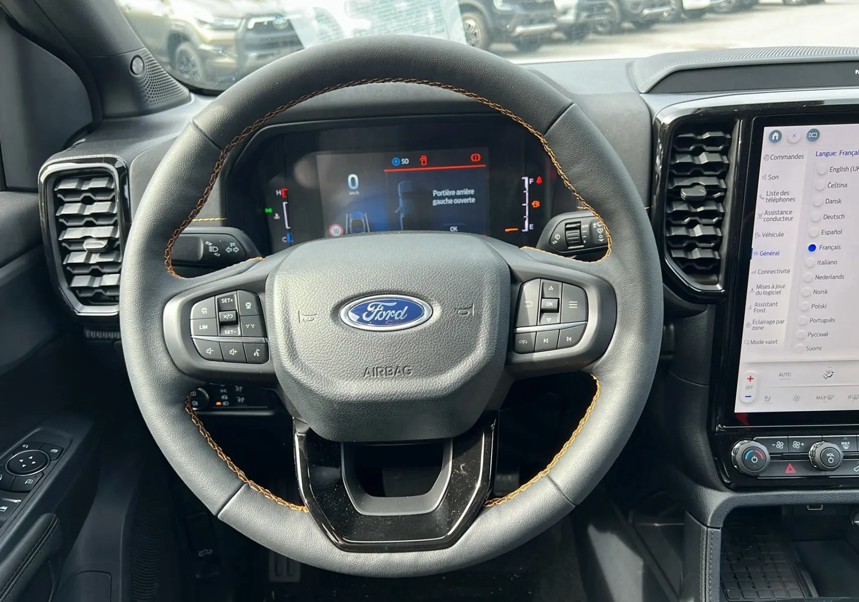 Vue intérieure centrée sur le volant cuir noir avec surpiqûres orange du Ford Ranger 2026, tableau de bord numérique et écran tactile.