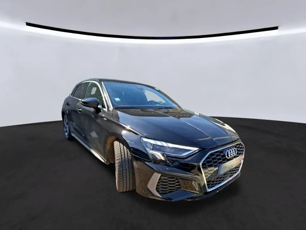Vue de face d'une Audi A3 Sportback noire 2023 avec calandre hexagonale et phares LED, en intérieur showroom.