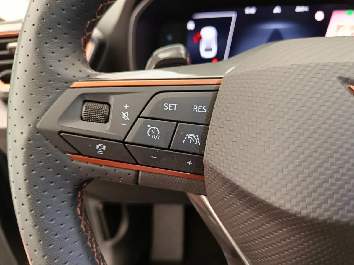 Gros plan sur la partie gauche du volant en cuir perforé noir avec surpiqûres orange de la CUPRA Leon ST 2024.