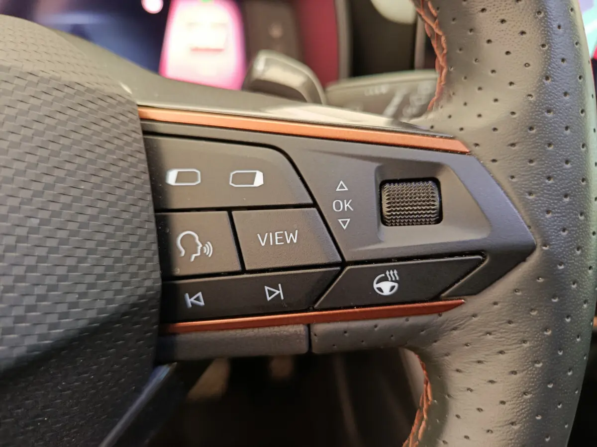 Gros plan sur les commandes gauche du volant perforé du CUPRA LEON ST gris foncé, avec boutons multifonctions et molette.