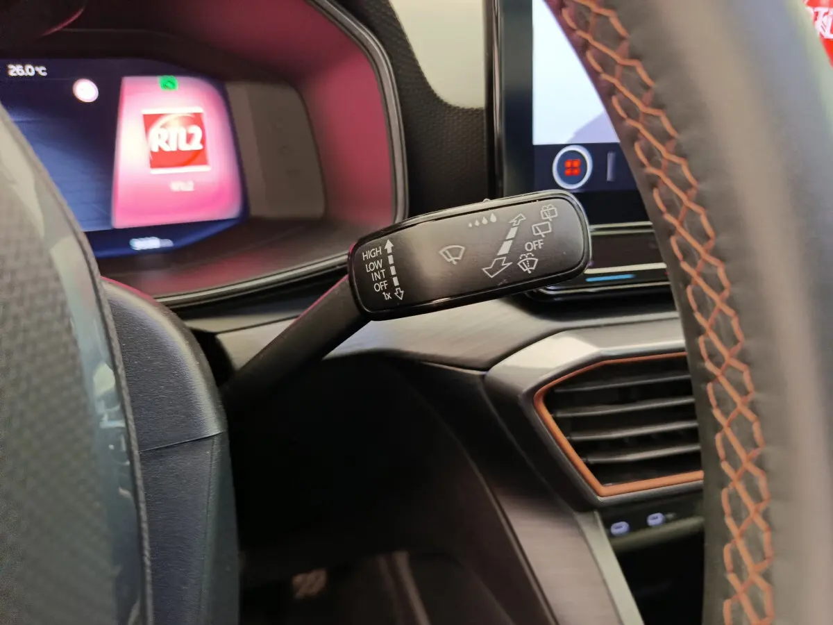 Gros plan sur la commande d’essuie-glace à gauche du volant cuir noir à surpiqûres orange du tableau de bord du CUPRA LEON ST 2024.