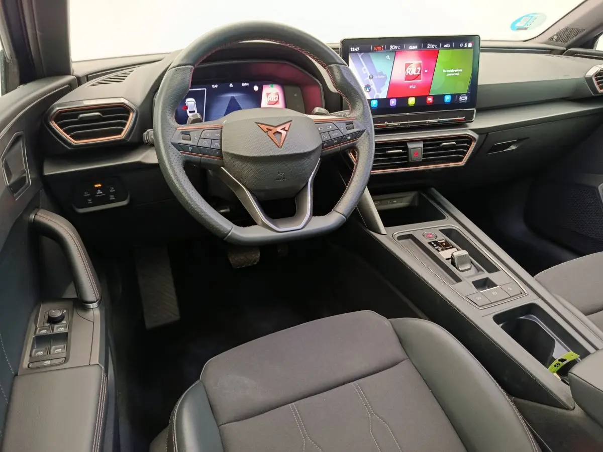 Intérieur de la CUPRA LEON ST 2024, vue du poste de conduite avec volant cuir, écran tactile 12 pouces et console centrale noire.