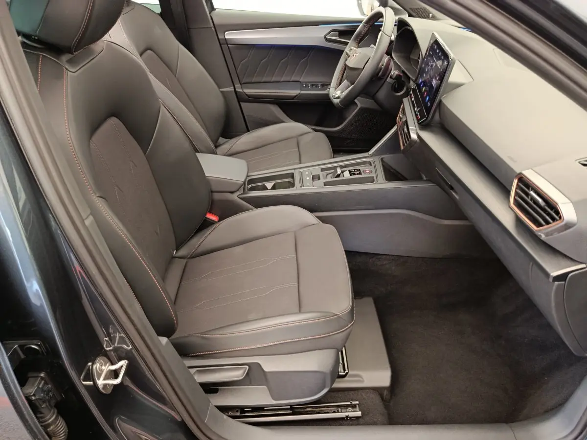 Intérieur côté conducteur de la CUPRA LEON ST gris foncé, sièges noirs avec surpiqûres orange et écran tactile central.