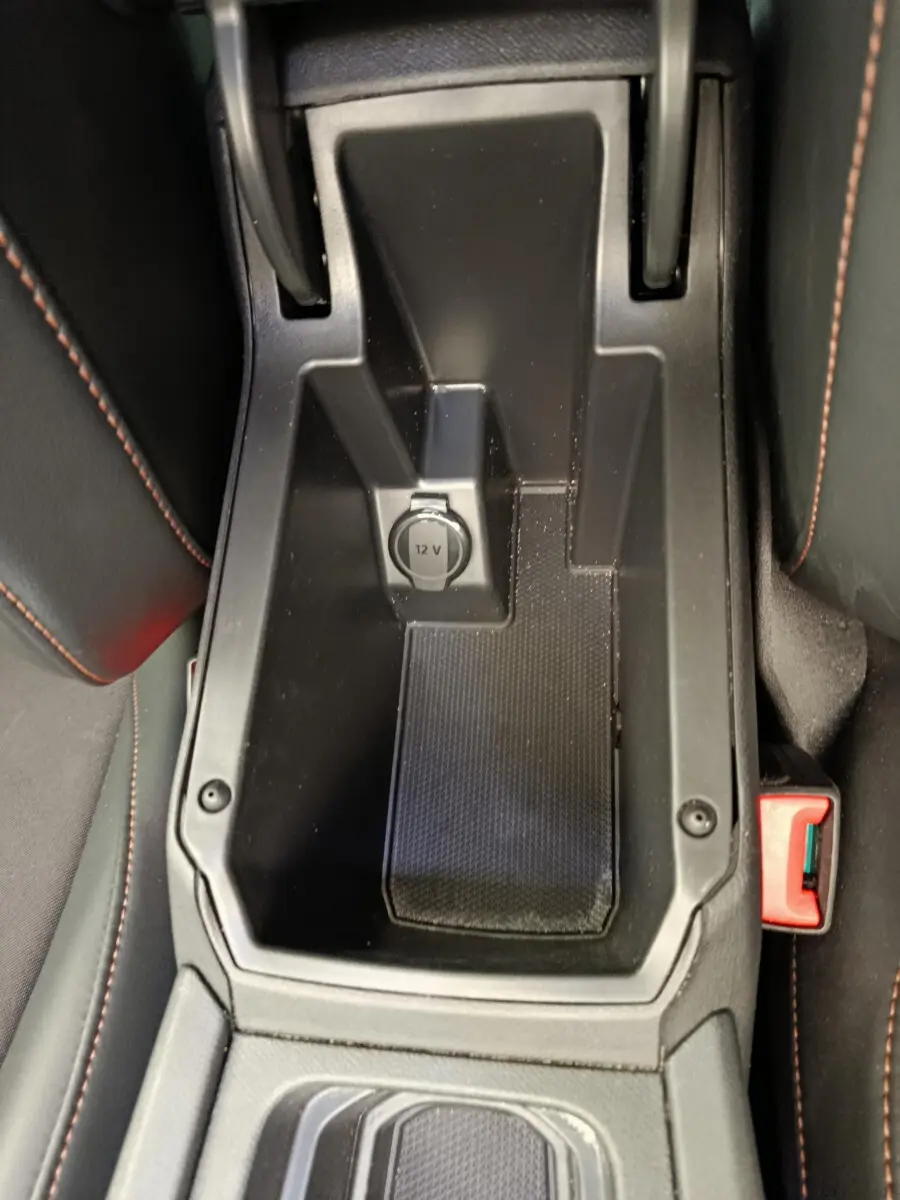 Vue plongeante sur le rangement central noir avec prise 12V et surpiqûres orange des sièges CUPRA LEON ST 2024.