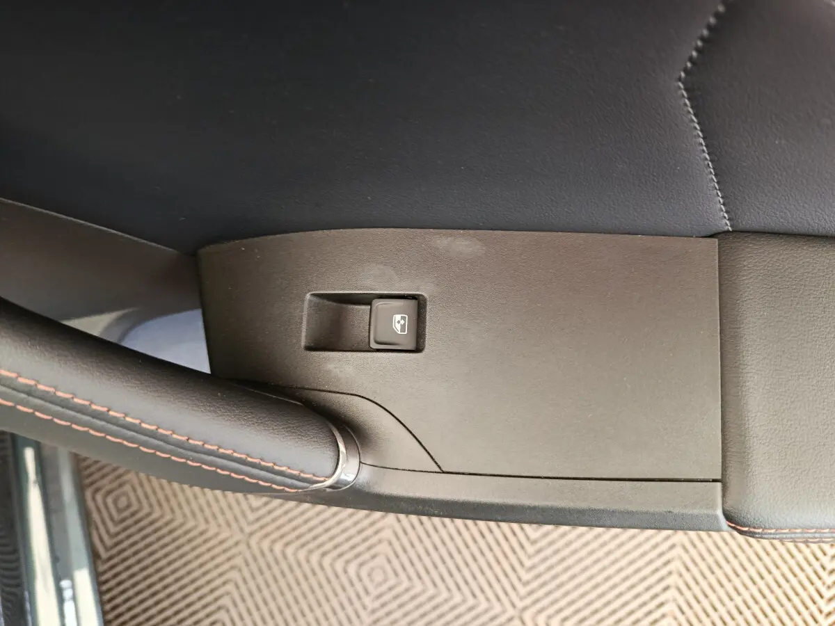 Gros plan sur le bouton de lève-vitre côté gauche dans l'intérieur noir avec surpiqûres rouges d'une CUPRA LEON ST 2024.