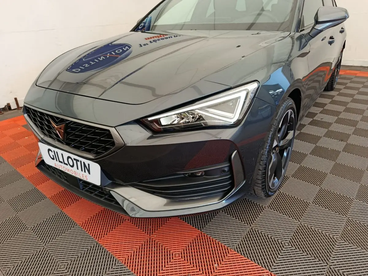 Vue 3/4 avant droit d'une CUPRA LEON ST gris foncé avec calandre noire et phares LED anguleux.