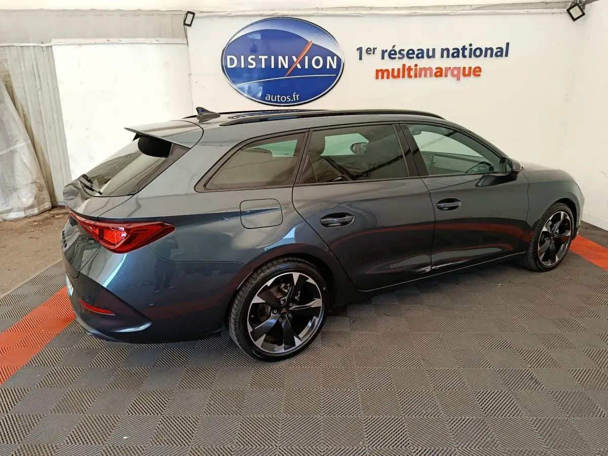 Vue 3/4 arrière droit d'une CUPRA LEON ST 2024 gris foncé avec jantes noires et toit ouvrant en intérieur showroom.