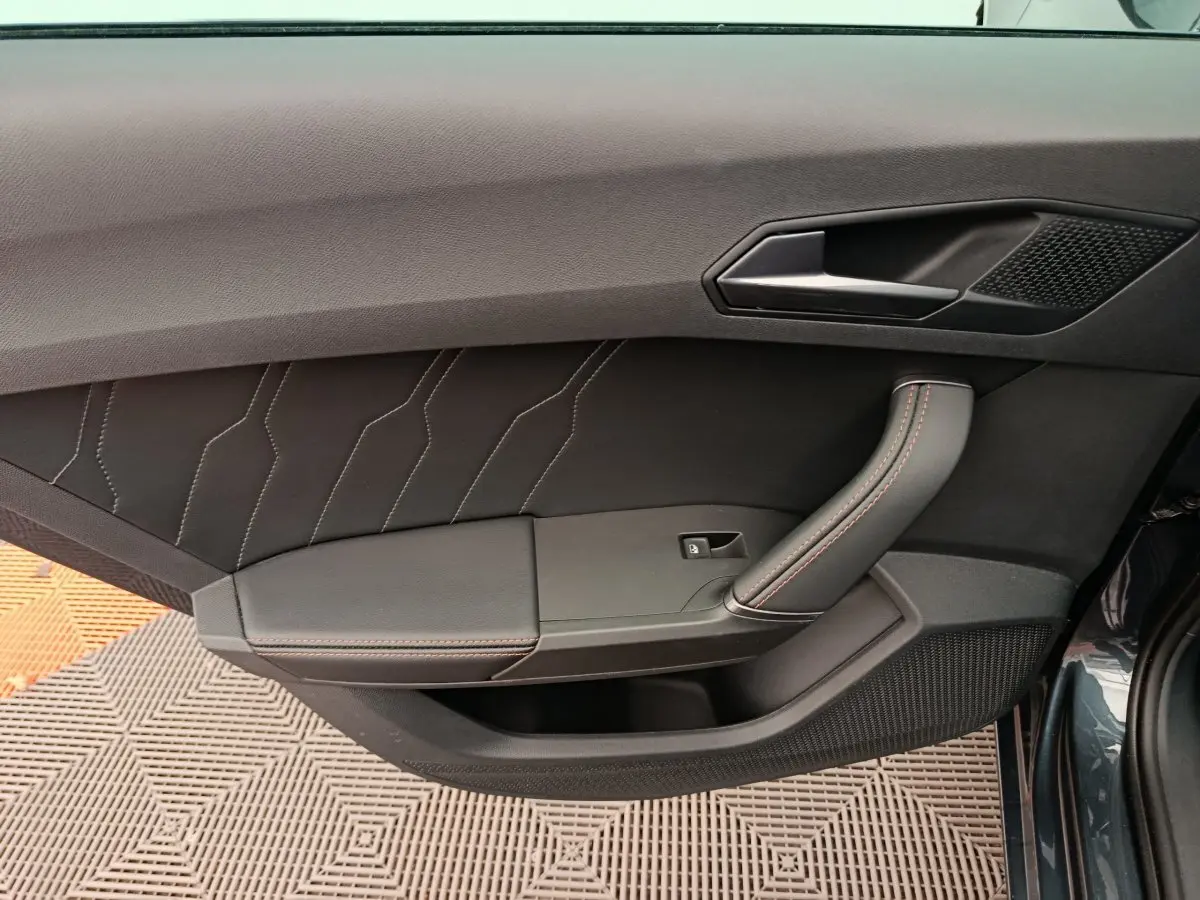 Porte intérieure côté gauche de la CUPRA LEON ST 2024 gris foncé avec surpiqûres rouges et poignée ergonomique.