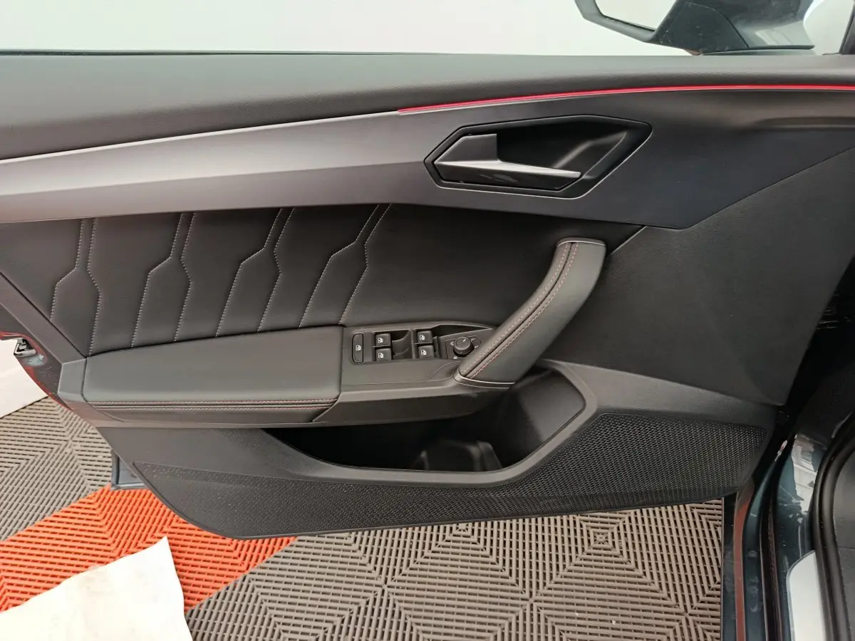 Vue côté gauche de la porte intérieure noire avec surpiqûres rouges et poignée en cuir du CUPRA LEON ST 2024 gris foncé