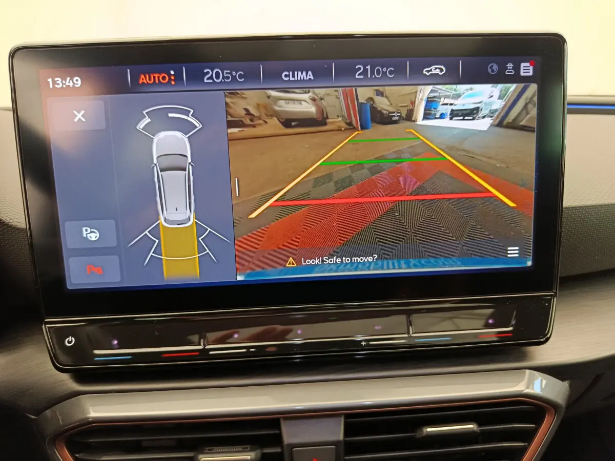 Écran tactile central montrant l'aide au stationnement arrière avec vue caméra sur tapis coloré, intérieur CUPRA Leon ST gris foncé 2024.