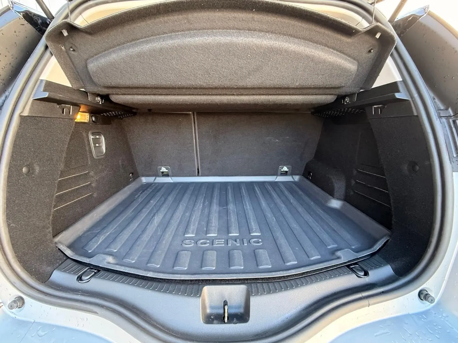 Coffre ouvert en vue arrière d’un Renault Scénic IV gris platine avec tapis de coffre marqué "SCENIC" et toit noir étoile.