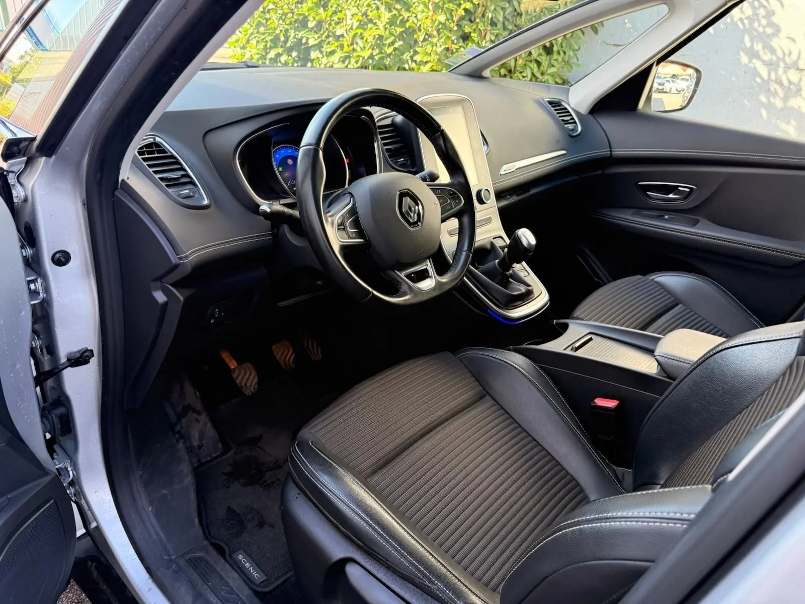 Intérieur avant gauche du Renault Scenic IV 2020 gris platine, volant cuir, tableau de bord moderne et boîte manuelle visible.