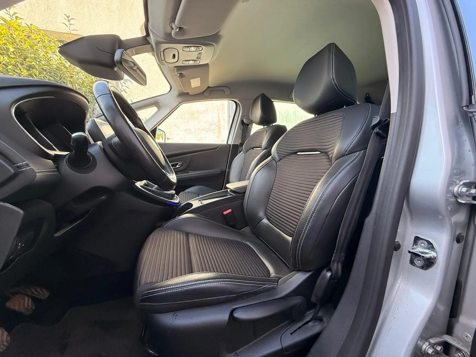 Vue intérieure côté conducteur du Renault Scenic IV 2020, sièges en cuir noir avec surpiqûres blanches et tableau de bord visible.