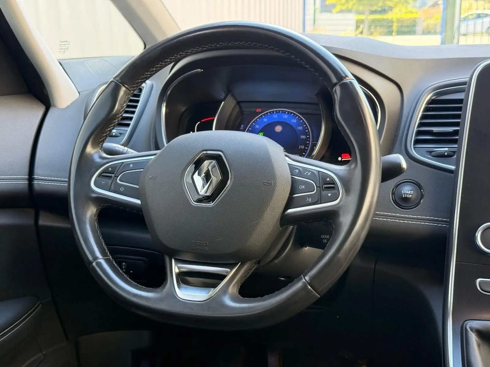 Vue rapprochée du volant noir avec logo Renault et tableau de bord digital du Scenic IV gris platine 2020.