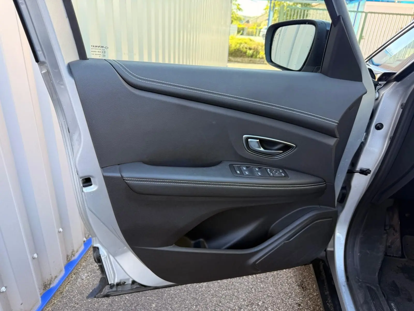 Porte avant gauche ouverte d'un Renault Scenic IV gris platine, avec garniture intérieure noire et commandes électriques.