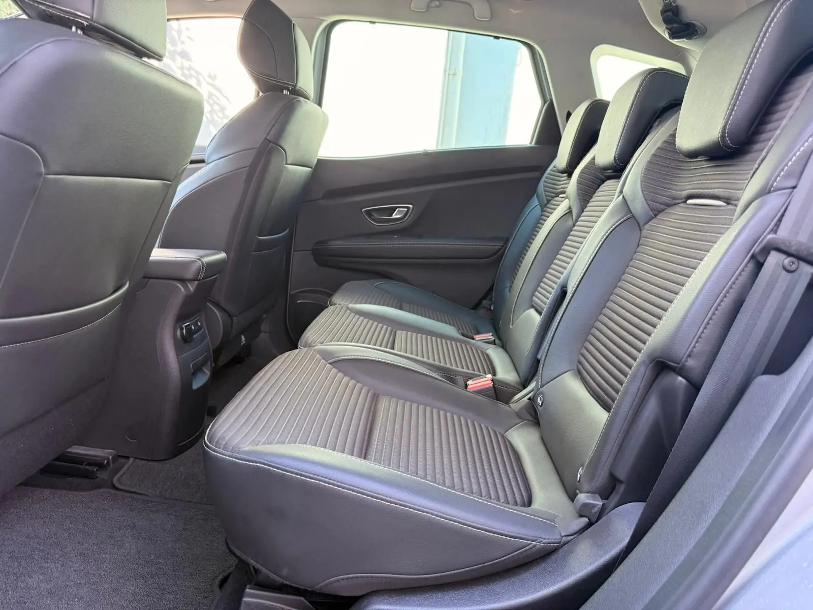 Vue latérale intérieure des sièges arrière en cuir noir du Renault Scenic IV gris platine, soulignant leur design moderne et confortable.