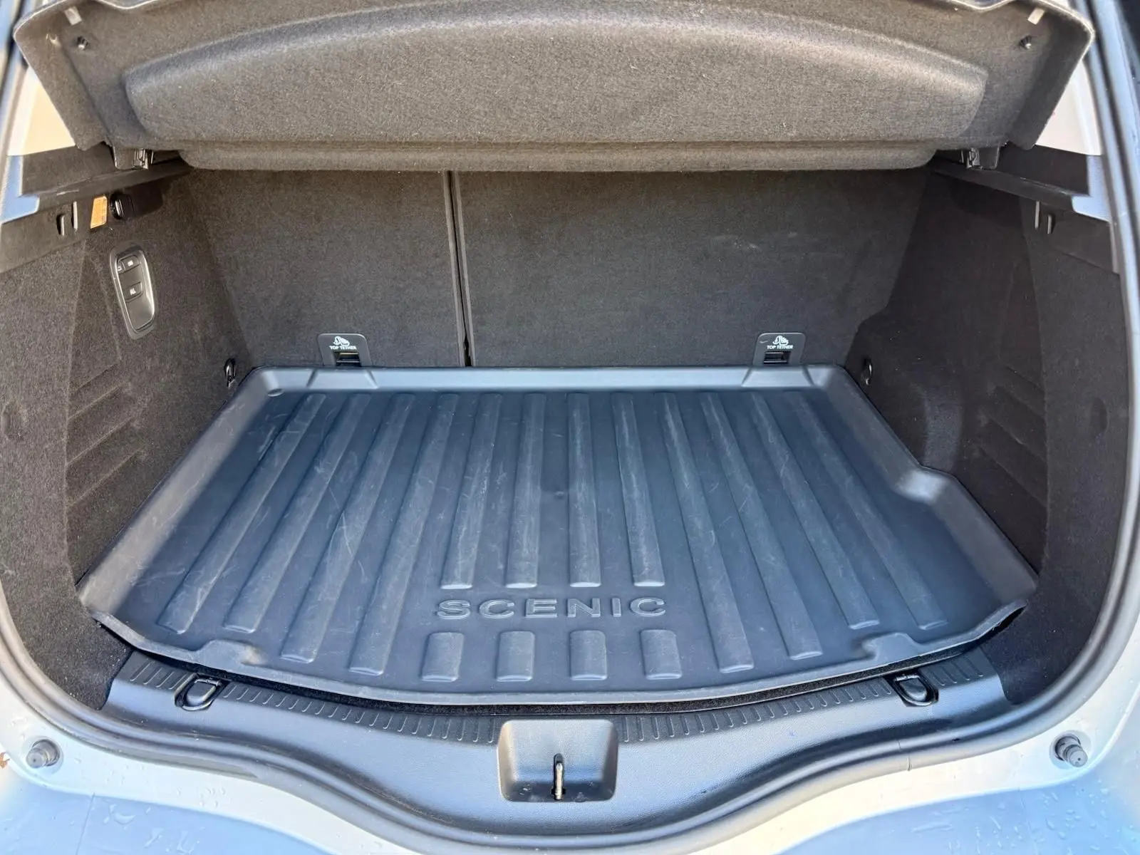 Coffre ouvert d'un Renault Scenic IV gris platine, vue arrière montrant le tapis de coffre marqué "SCENIC".