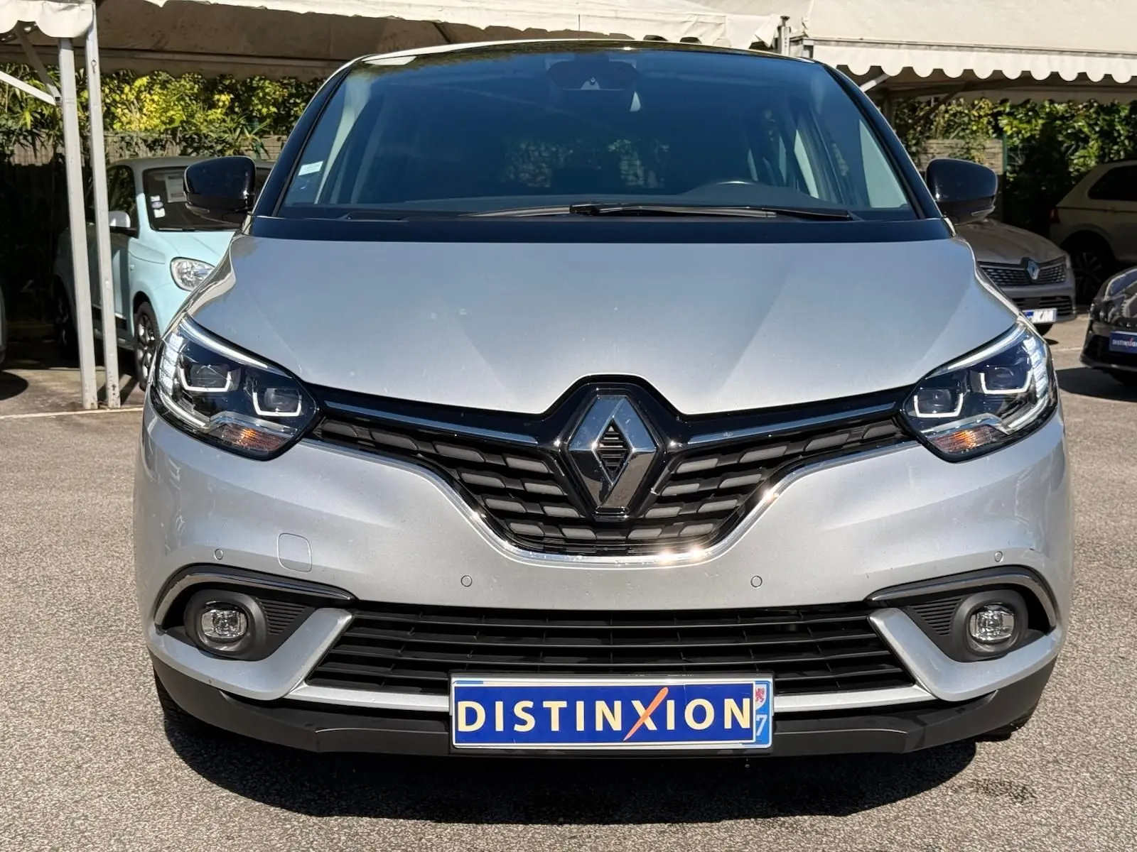 Vue frontale d'un Renault Scénic IV gris platine avec toit noir, mettant en valeur sa calandre et ses phares LED.