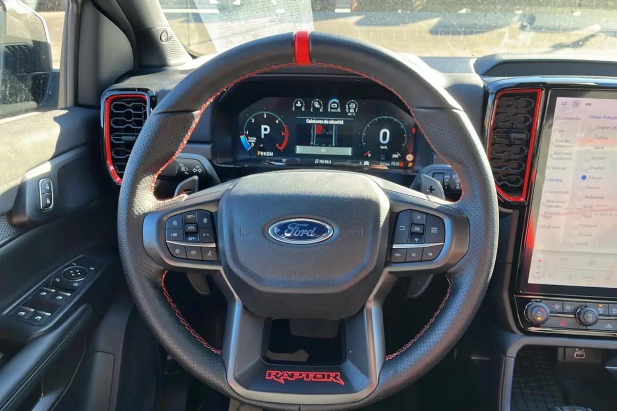 Vue intérieure centrée sur le volant cuir noir avec surpiqûres rouges et logo Raptor rouge du Ford Ranger Raptor 2025.