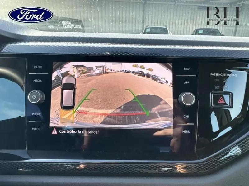 Écran tactile affichant la caméra de recul avec vue arrière et lignes de guidage sur un Volkswagen Taigo blanc.