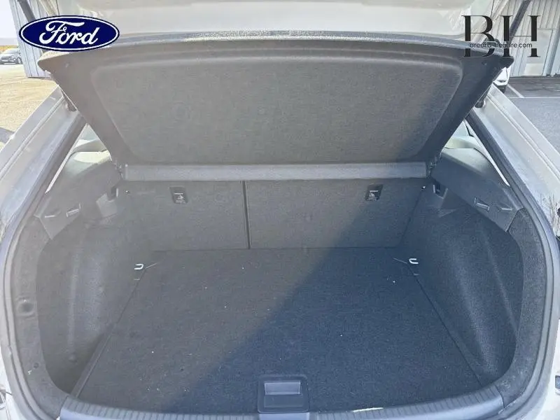 Coffre ouvert vu de l'arrière d'un Volkswagen Taigo blanc, espace de chargement vide et tapis noir.